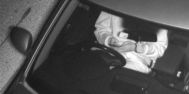 Grainy b&w image of a person holding their phone while driving