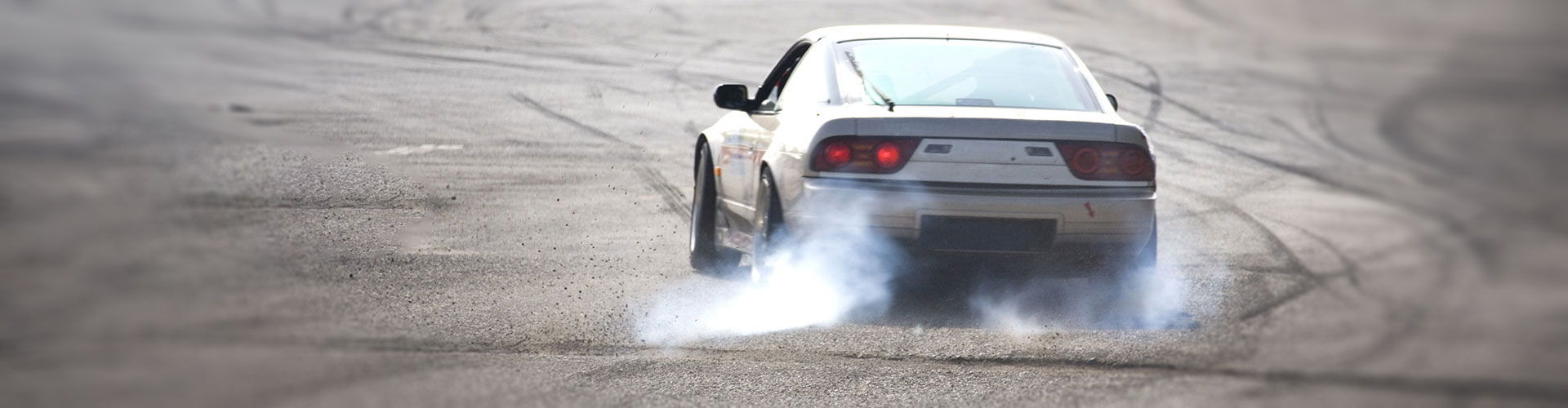 A white car doing burnouts in a skid-marked parking lot