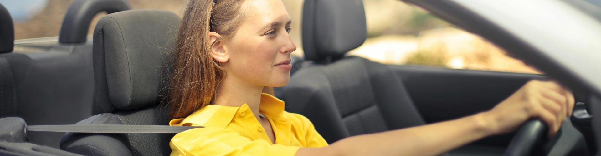 Woman in yellow top sits in drivers seat of a convertible car