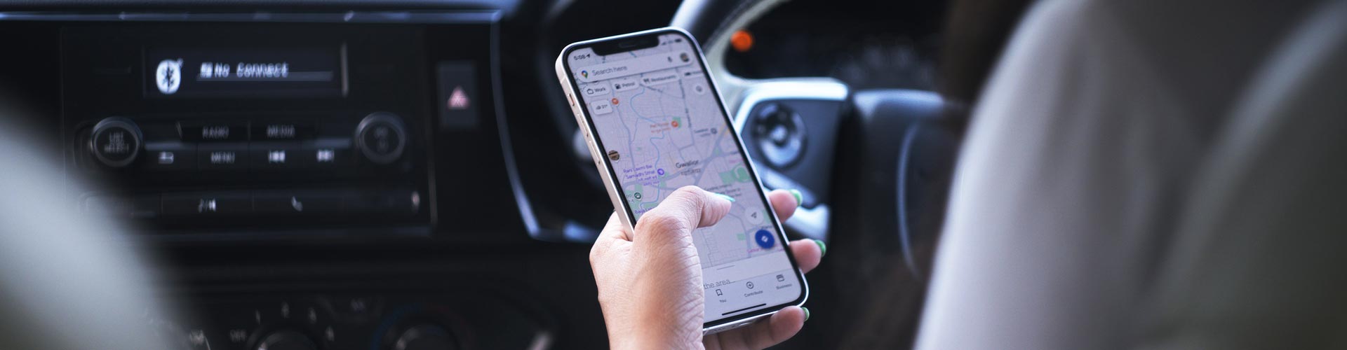 A woman's hand holds a phone while she is in the driver's seat