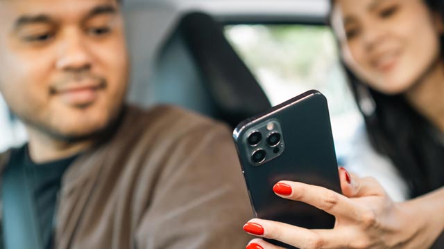 A woman in the back seat of car shows the driver something on her mobile phone