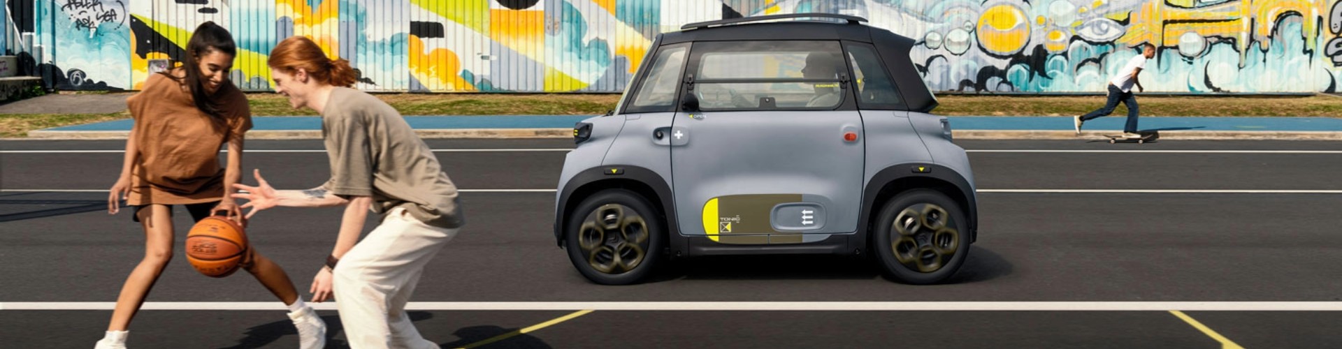 Two young people play basketball in front of a Citroen Ami micro-ev