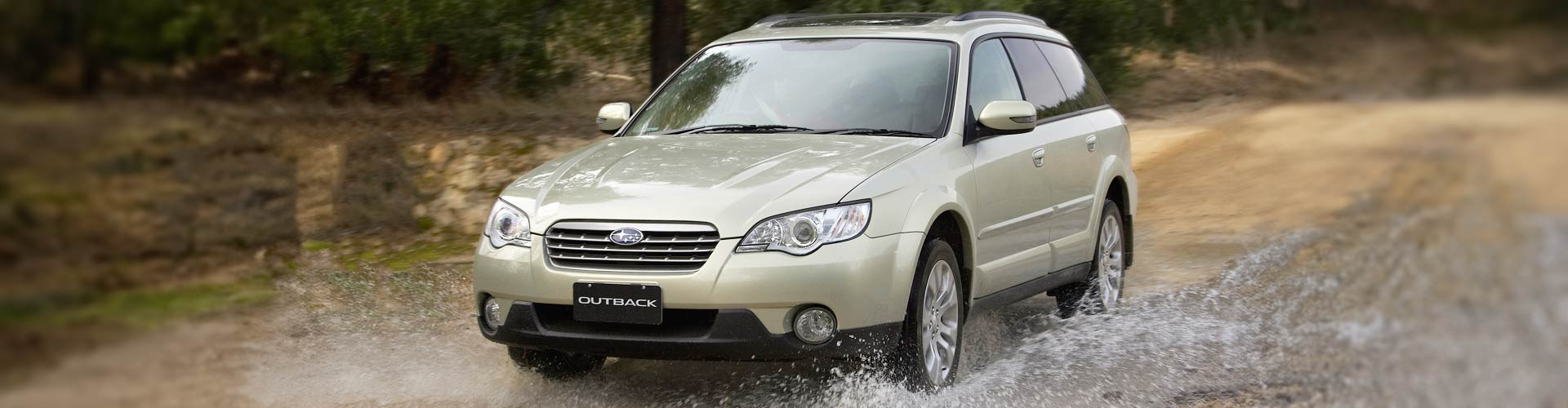 Gold 2004 Subaru Outback driving through a puddle on a dirt road