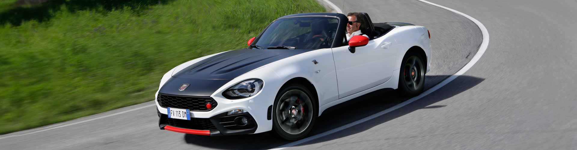 Man driving sports car with the top down with metallic, white with black stripe paint colour with black wheels