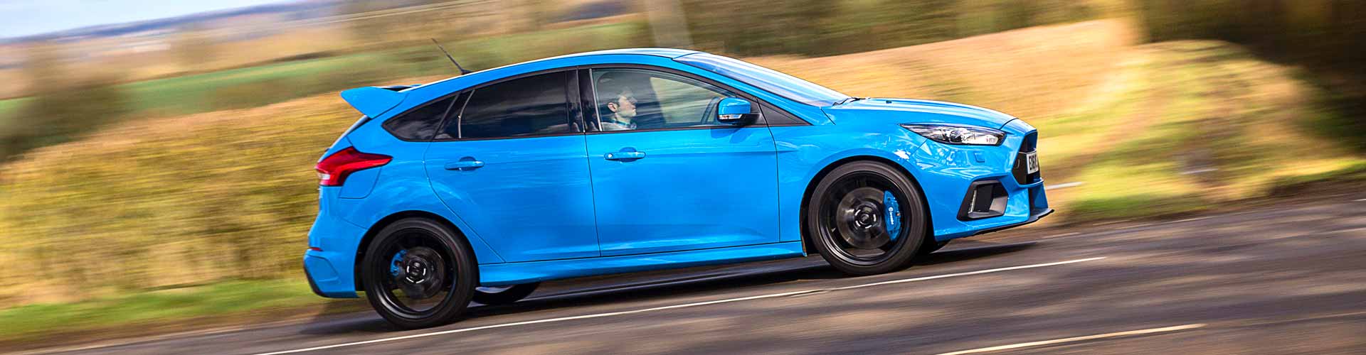 Blue 2016 Ford Focus driving uphill against yellow grass