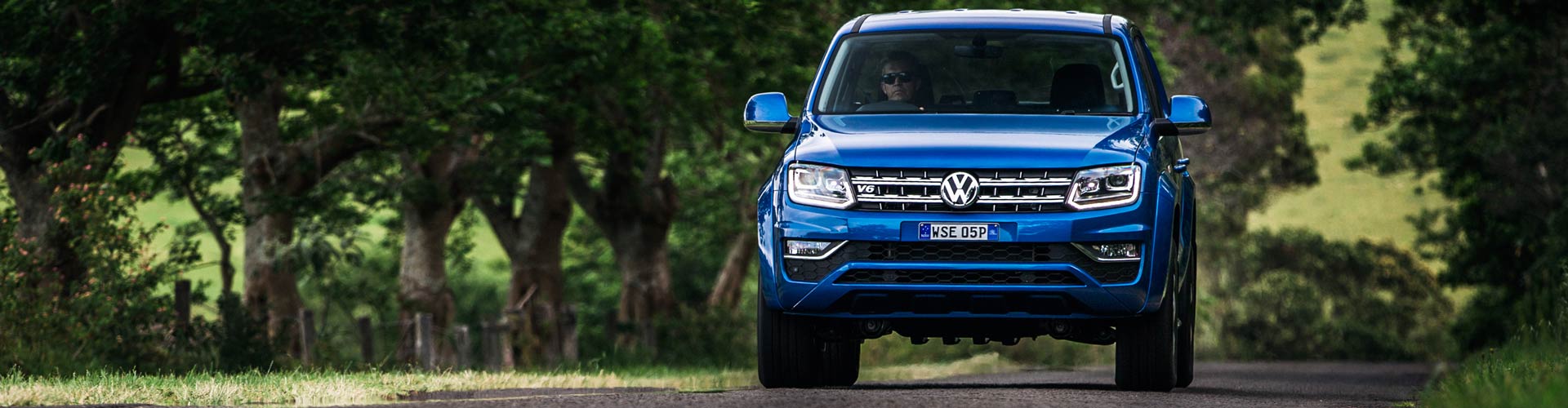 A blue 2016 Volkswagen Amarok V6 driving towards the viewer on a country road