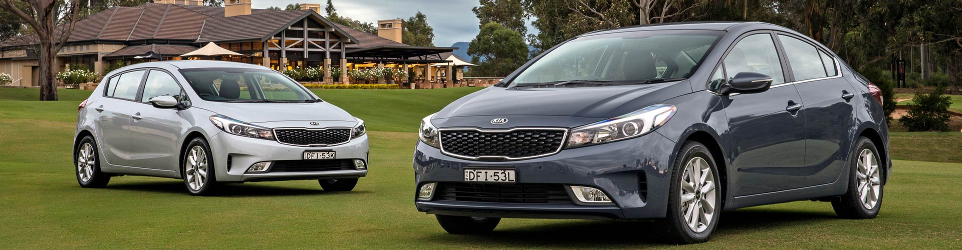 Two Kia Cerato cars parked on a lawn in front of a big house