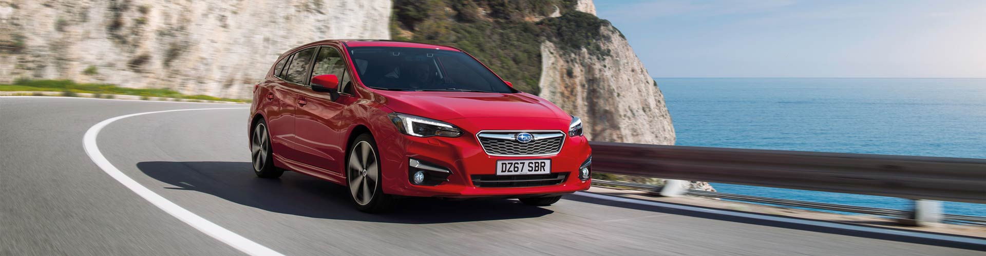 Red Subaru Impreza driving on coastal road with cliff in background