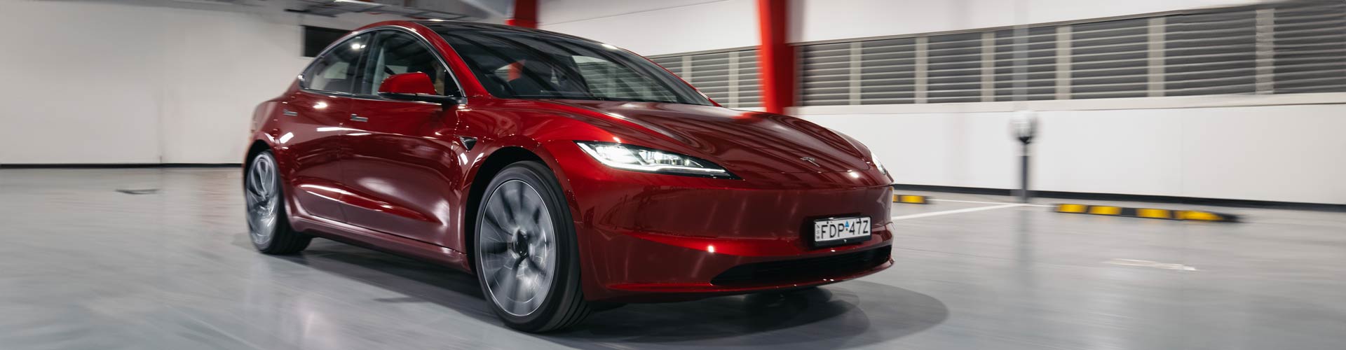 Red 2024 Tesla Model 3 driving inside a showroom
