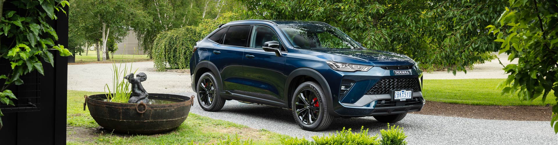 2025 GWM Haval H6GT PHEV parked in driveway surrounded by green plants