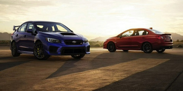 A red and a blue car parked side-by-side beside a road with a sunset in the background.