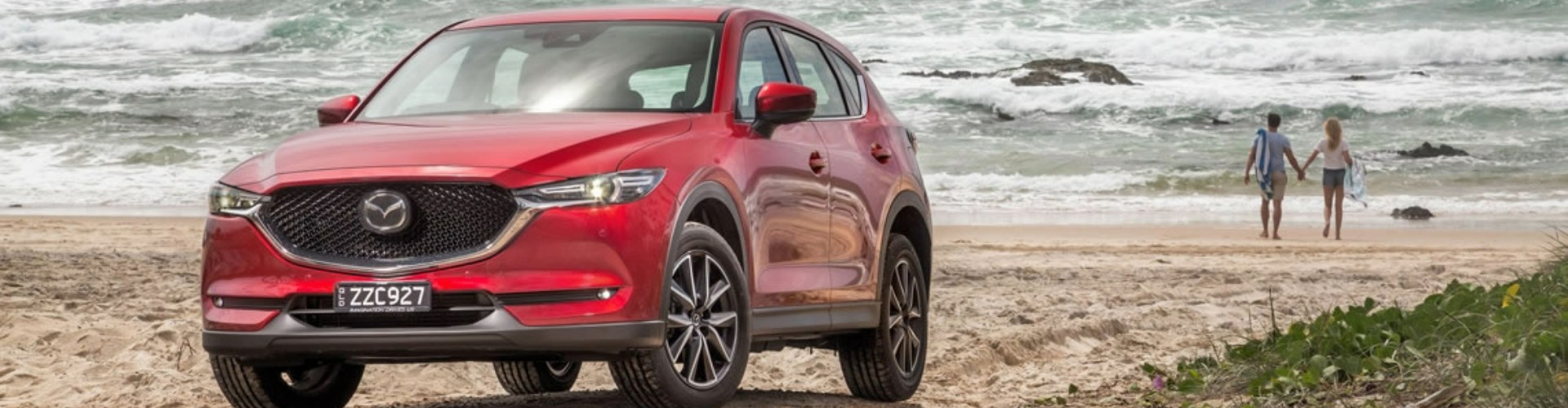 Front view of a red Mazda SUV parked on sea sand close to shore.