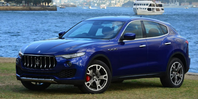 A blue Maserati SUV parked in front of a harbour.