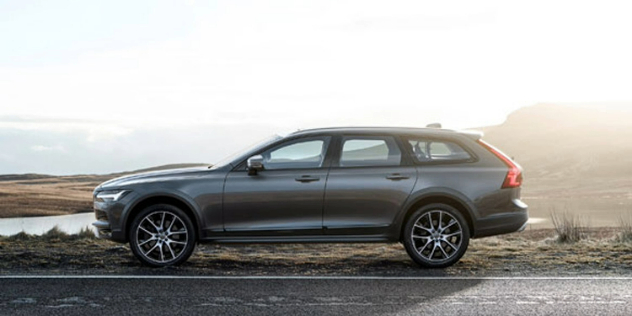 Side-angle view of a grey Volvo parked alongside a road with mountain terrain in the background.