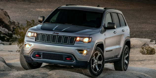 Front-angle view of a silver Jeep SUV parked on rocky terrain.