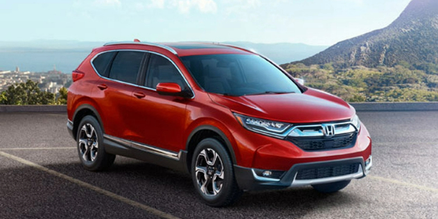 Side-angle view of a red Honda SUV with a blue skyline and mountain in the background.