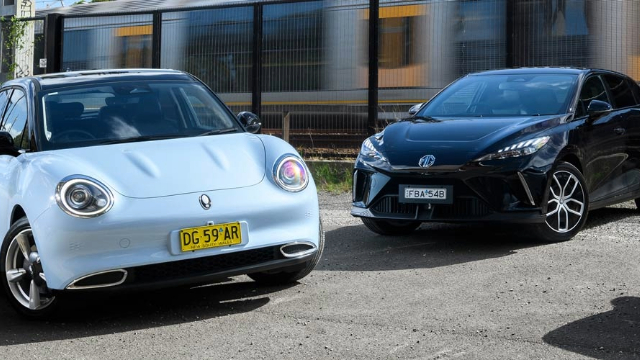 Three-EVs-MG-GWM-BYD-640x360 Three cars parked next to each other in front of a train line.