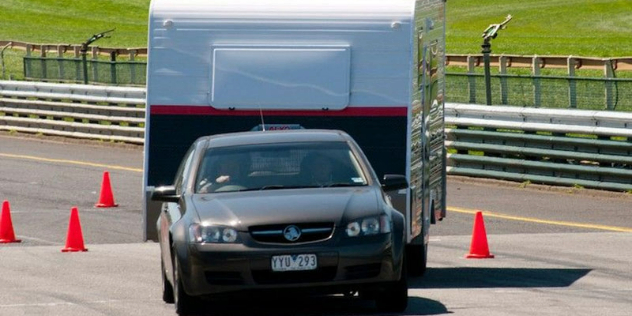 A sedan towing a caravan through a windy test course