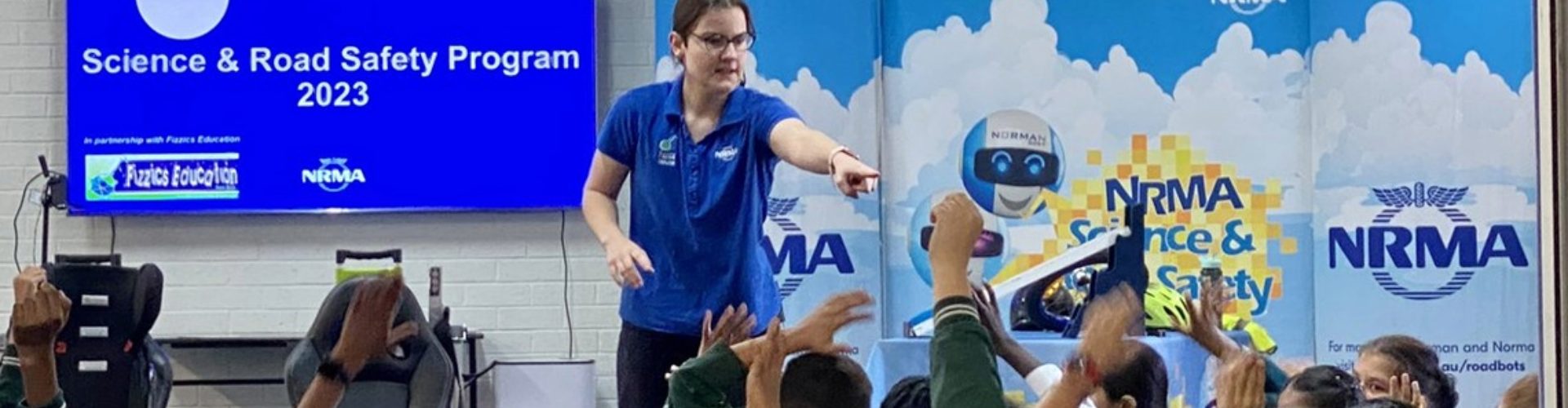 An NRMA educator stands at the front of a classroom of young people with their hands up