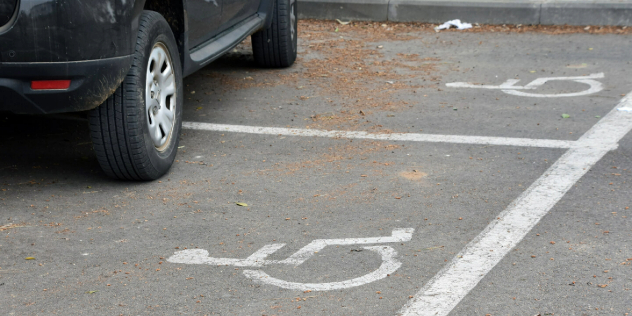 View of the wheels of a car parked incorrectly across two disability parking spaces