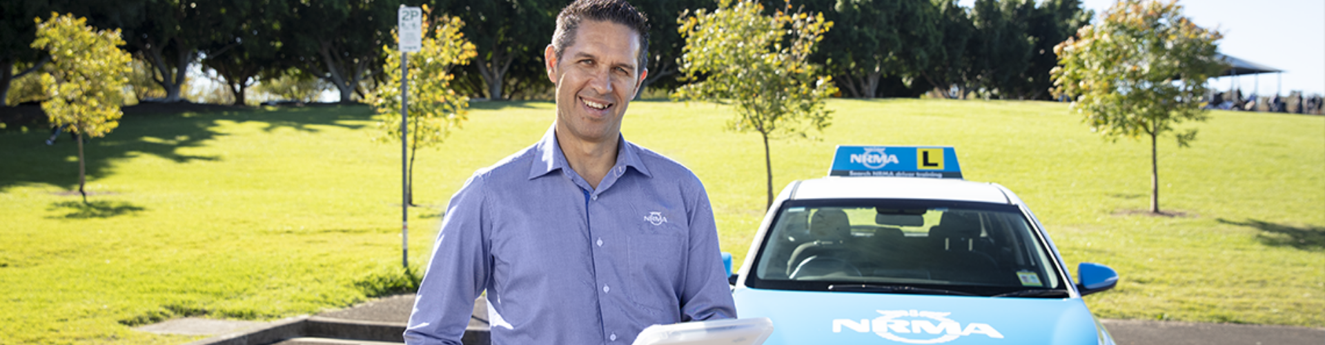 An NRMA driving instructor standing in front of a parked NRMA driving instruction vehicle An NRMA driving instructor standing in front of a parked NRMA driving instruction vehicle