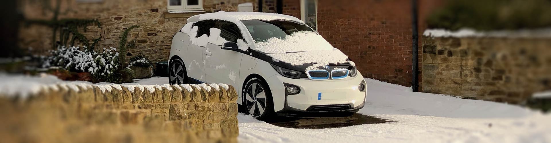 2017 BMW i3 covered partially in snow parked in a driveway next to a rock wall