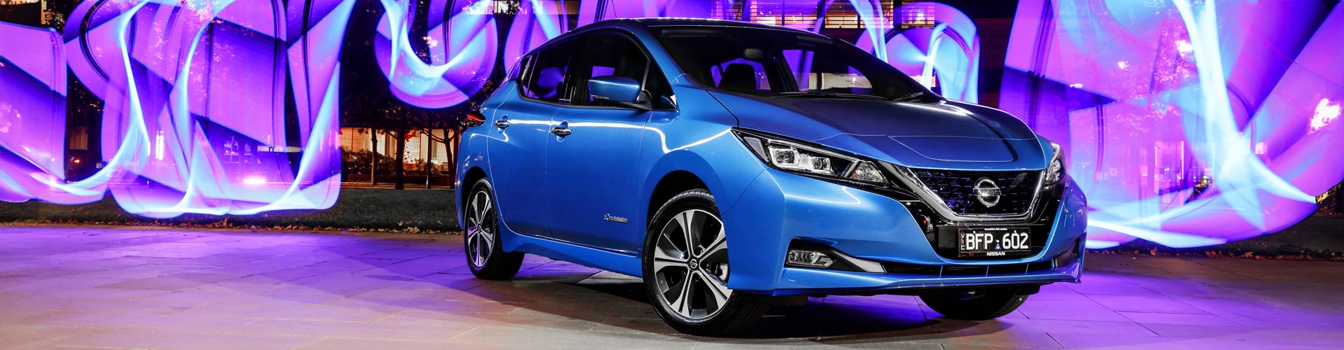 Blue Nissan Leaf e+ parked in front of neon sign