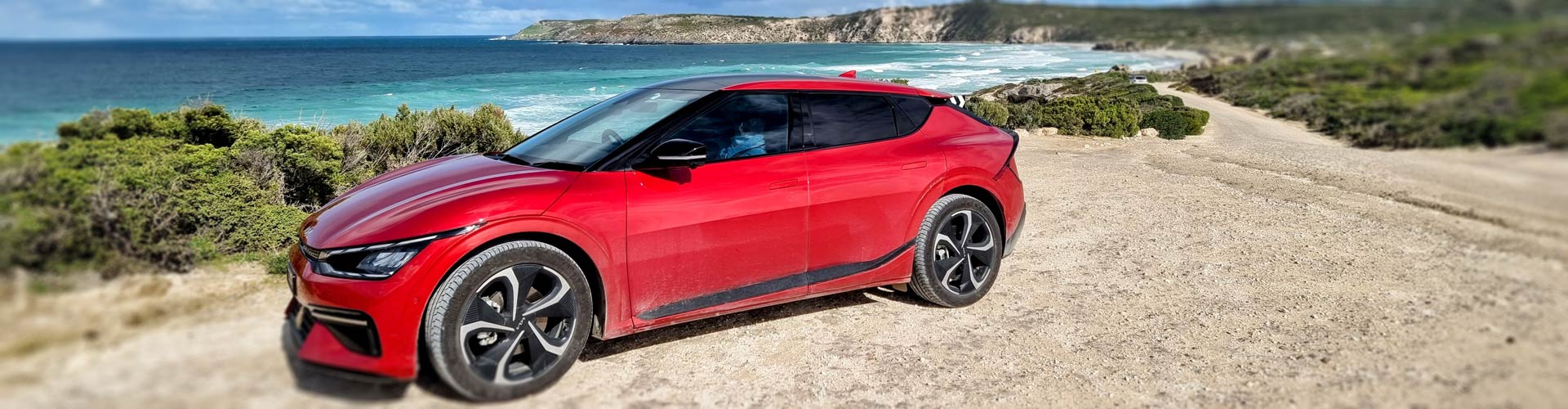 Red 2022 Kia EV6 GT Line parked near beach with rocky headland in background