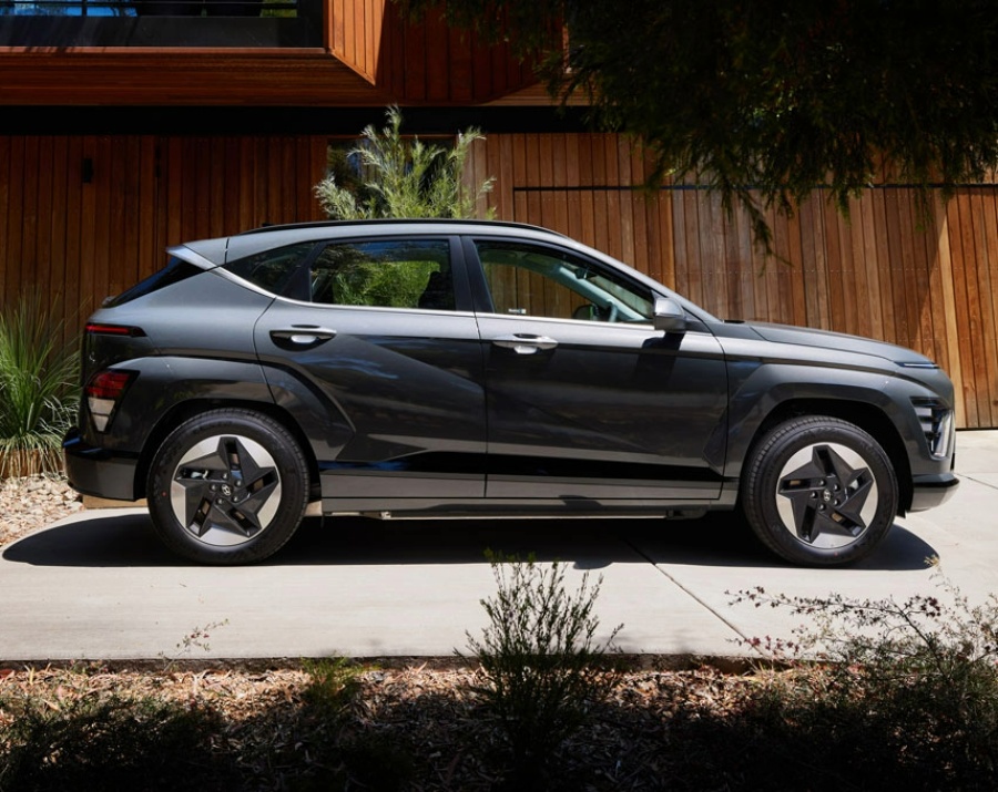 Side view of a grey suv parked on a concrete driveway next to a house made from wooden slats.