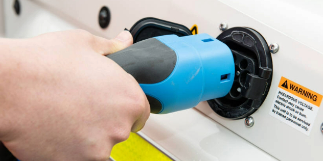 Hand plugging an electric charger into a white car.