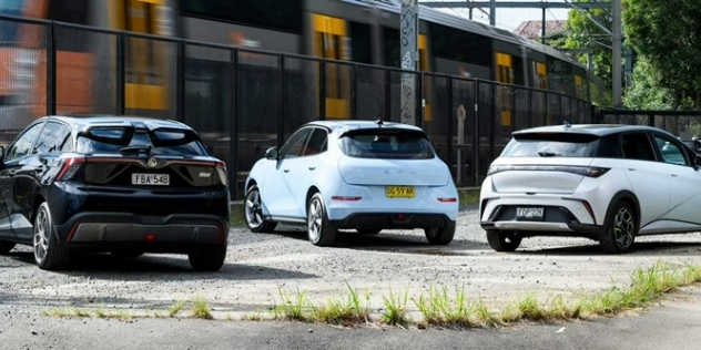 Rear view of three electric hatchback cars parked alongside a railway line.