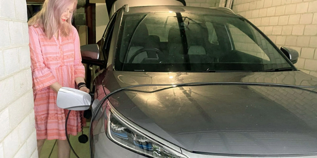 Lady standing in an enclosed space, plugging a charging cable into the front left side of a car.