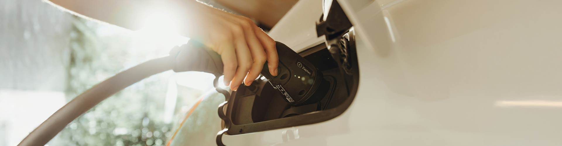 A hand plugs in a white EV with a curly cable