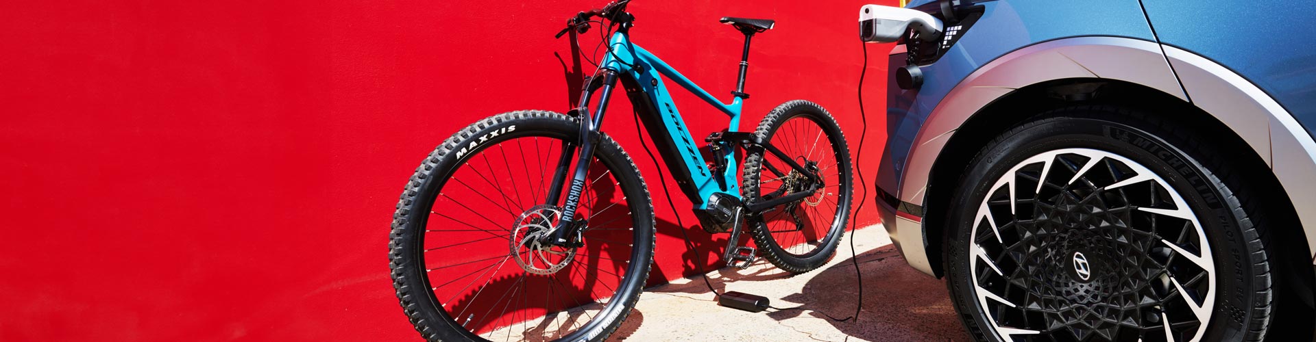 A Hyundai Ioniq 5 charges an e-bike against a red wall