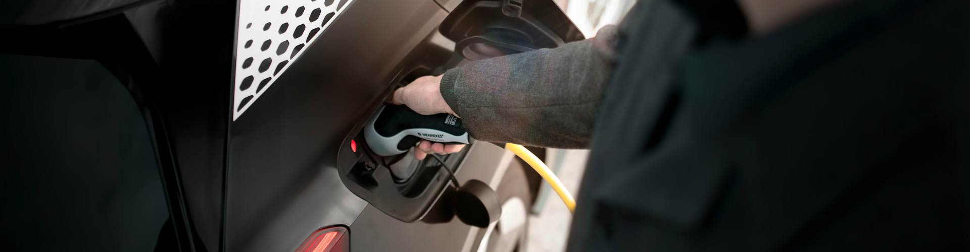 Arm of person in grey sleeve charging a black EV