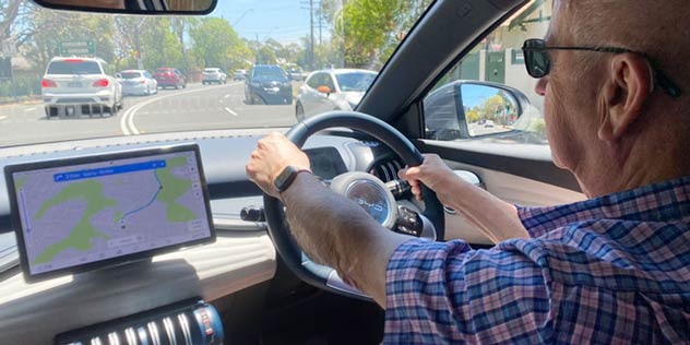 Rear view of a man sitting in the driver's seat, holding the steering wheel and looking forward.