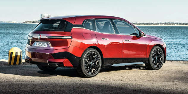 Side-angle view of a shiny, new, red 2022 BMW iX parked beside the ocean on a dock.