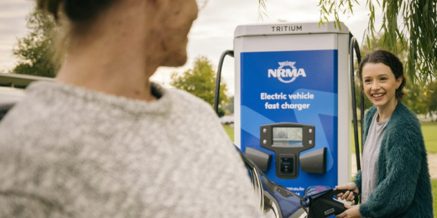 A young girl holding charging an electric vehicle while looking at another person and smiling.