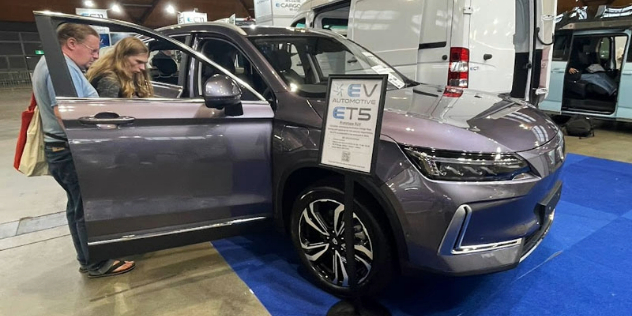 Two people looking at a grey ETV parked in a brightly lit exhibition car show area.