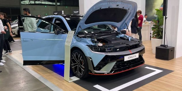 A powder blue Ioniq 5 parked in showroom with its front driver's side door and bonnet open, showcasing the the engine.