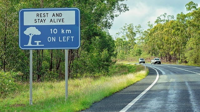 Front view of a 'Rest and stay alive' sign beside a road.