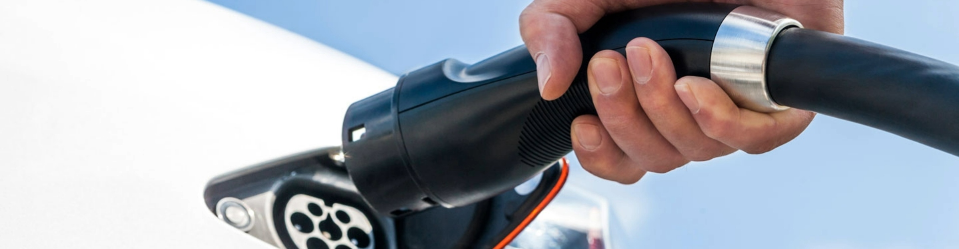 A hand holding an EV charging cable and about to plug into a white car.