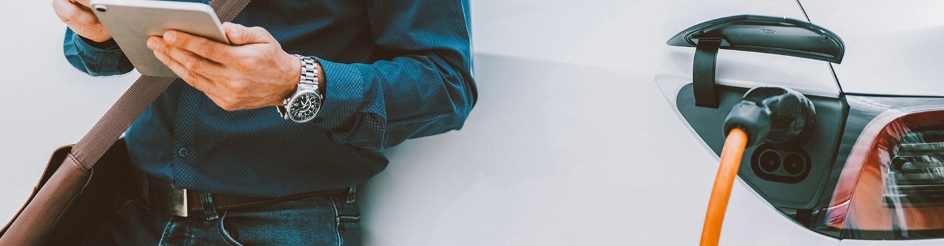 Someone reads their tablet while waiting beside their charging EV