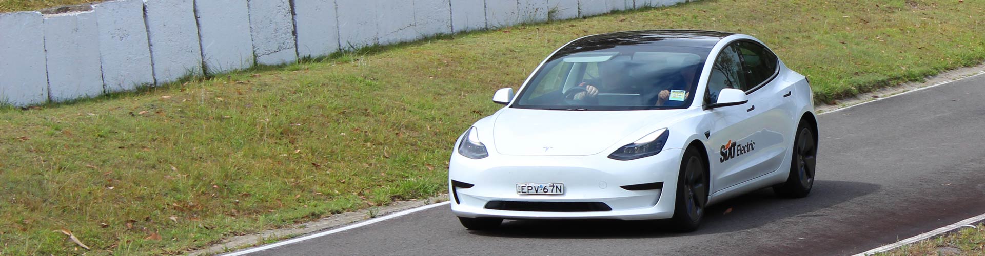 A white Tesla EV with a SIXT logo on the side driving on a track