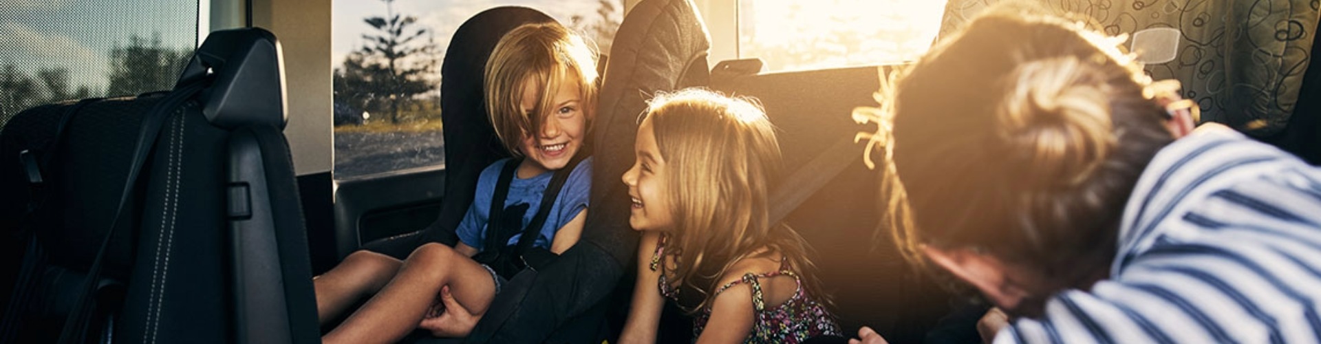 A parent reaches in to back of car to secure children in their seats
