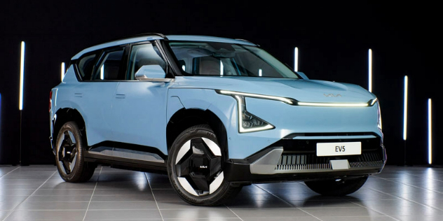 A powder blue KIA SUV parked in a dark showroom with fluorescent strip lights on the walls.