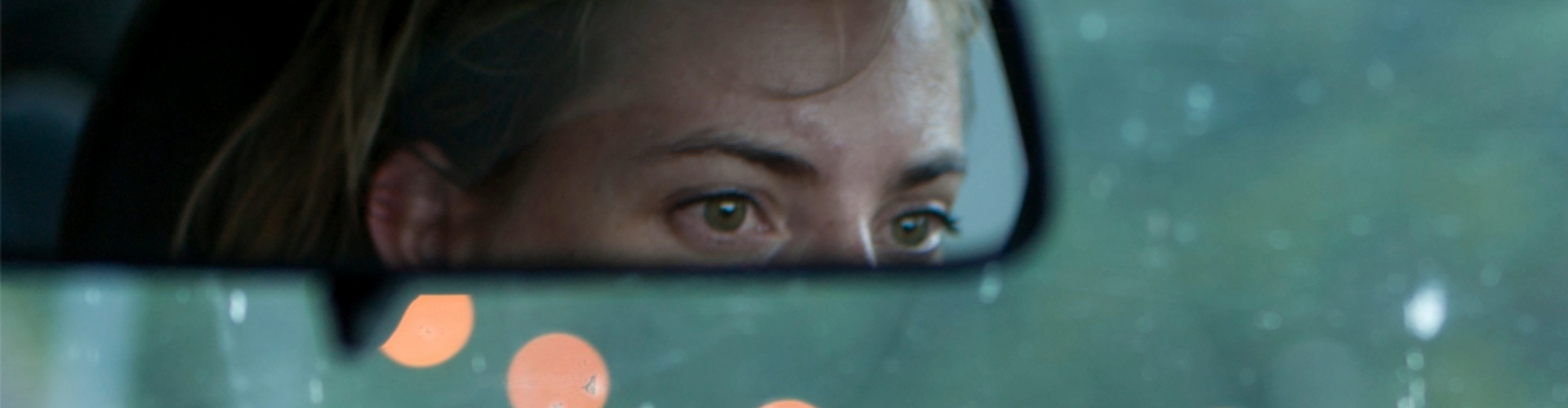 Reflection of the top half of a woman's face in the car review mirror.