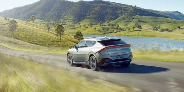 A Kia EV drives along a picturesque country road