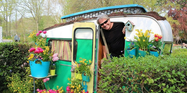 Side view of a retro caravan with an occupant standing in the doorway smiling