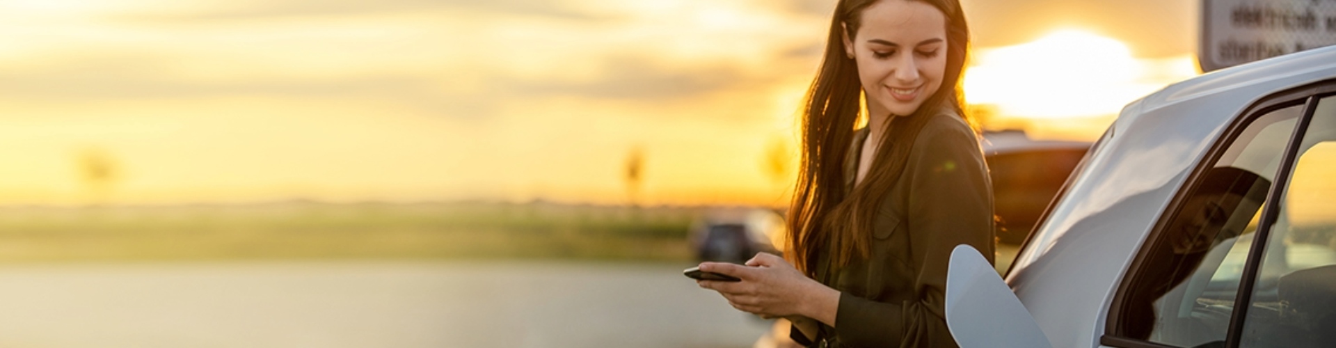 A smiling person leans against their EV while it charges